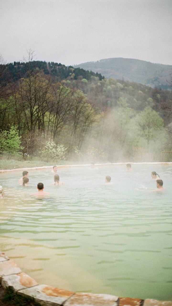 Steam rising from a warm mineral pool ringed by beech trees in the Berehove basin